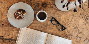 Pair of Daniella reading glasses propped beside a cup of coffee and magazine